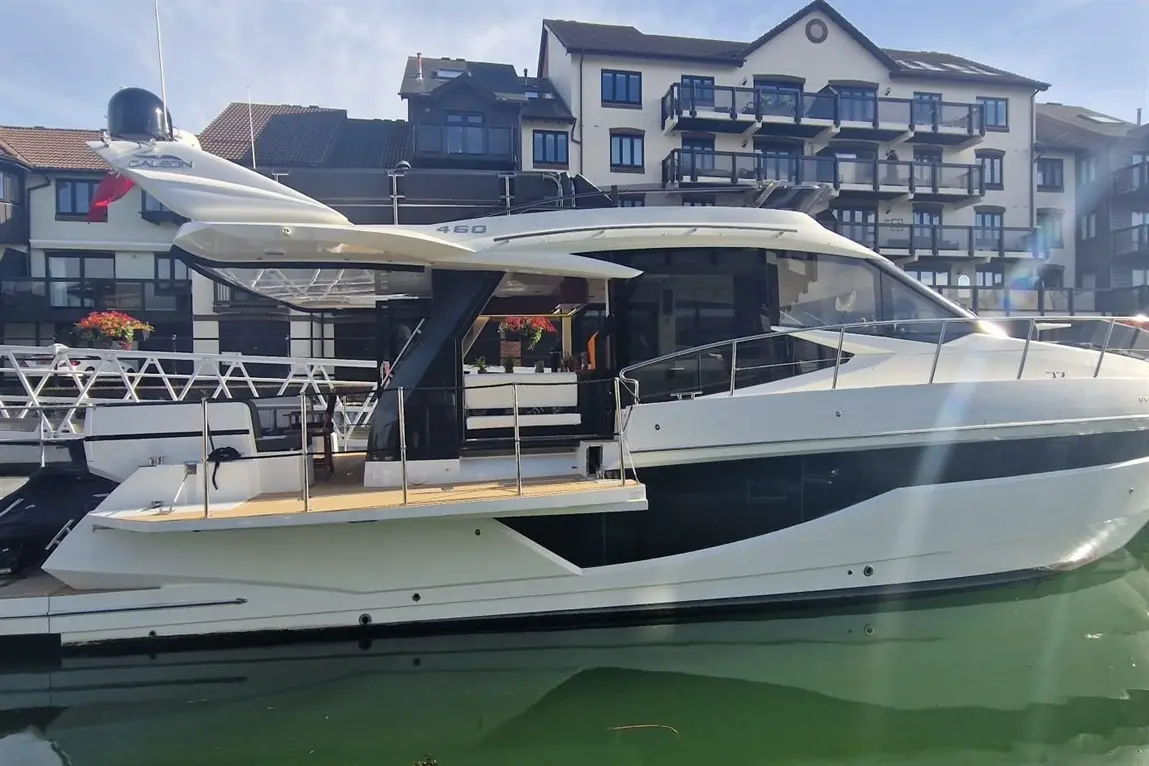 Luxury motorboat moored at a marina, featuring a sleek design and the number "460" on the side, with modern buildings in the background.